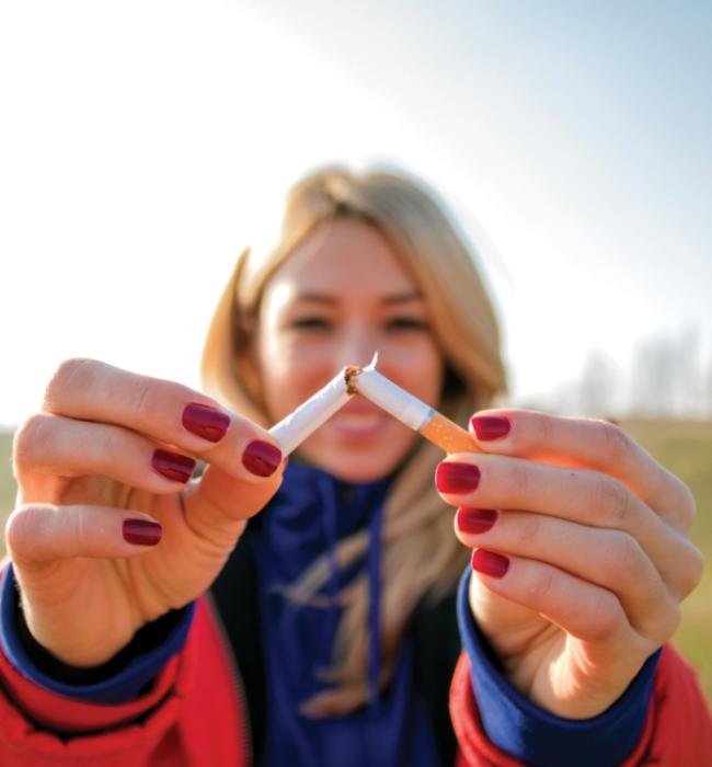 A woman holding up her hands in focus and breaking a cigarette in half.