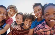 A collection of young children, male, female, Black, white, and Latinx hugging and smiling at the camera