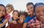 A collection of young children, male, female, Black, white, and Latinx hugging and smiling at the camera