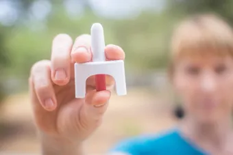 A photo of a white woman holding a dose of Narcan up to the camera. The Narcan and her hand are in focus; her face is blurry.