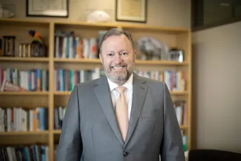 Headshot of Jay Bernhardt, Ph.D., MPH, former Dean of Moody College of Communication, current President of Emerson College, and founding director of the Center for Health Communiation at The University of Texas at Austin. A white man with a graying beard in a gray suit and orange tie.