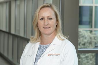 Headshot of Alison Cahill, a white woman with shoulder-length blonde hair wearing a white doctor's coat and smiling at the camera.
