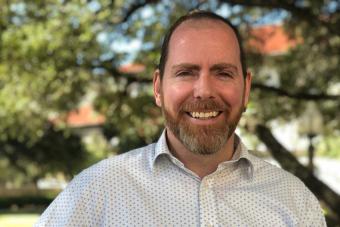 Headshot of Brad Love, a white man with very short brown hair and a beard wearing a button down shirt and smiling at the camera.