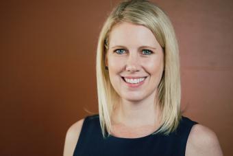 Headshot of Kate Pounders, a white woman with shoulder-length blonde hair and blue eyes in a black sleeveless dress smiling at the camera