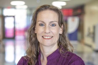 Headshot of Rene Dailey, a white woman with long, curly brown hair and blue eyes in a purple top smiling at the camera