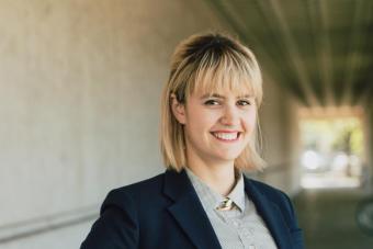 Headshot of Laura Brown, a white woman with shoulder-length blonde hair and brown eyes wearing a blue polka dotted button down shirt, a navy blazer, and smiling at the camera