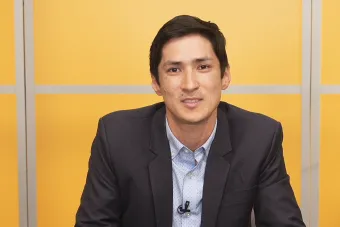 A photo of Dr. Greg Wallingford sitting down in front of a yellow background looking at the camera.