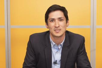 A photo of Dr. Greg Wallingford sitting down in front of a yellow background looking at the camera.