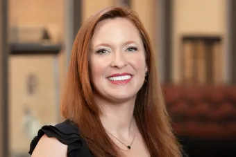 A headshot of Dr. Ashley Garling, a white woman in her 40s with long red hair wearing a black top and smiling at the camera.