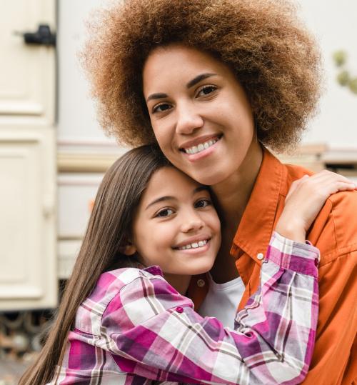 A young Black mother and her daughter hugging and smiling at the camera