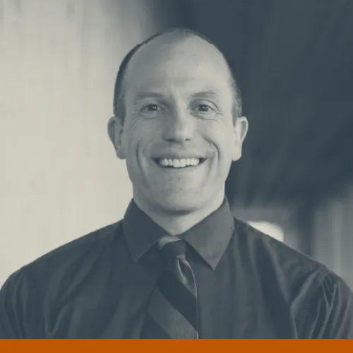 Headshot of Mike Mackert, a bald, white man in his 40s wearing a dress shirt and tie and smiling at the camera.